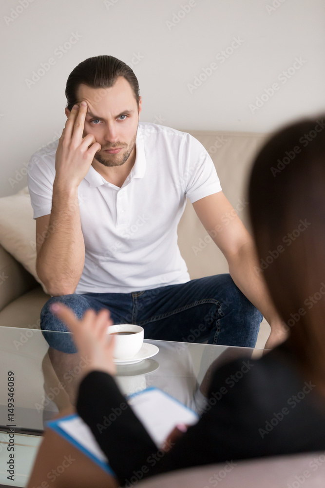 Serious concerned male patient sitting on the couch listening attentively to advices of psychotherapist, businessman negotiating with female partner, meeting with lawyer or financial advisor Serious concerned male patient sitting on the couch listening attentively to advices of psychotherapist, businessman negotiating with female partner, meeting with lawyer or financial advisor