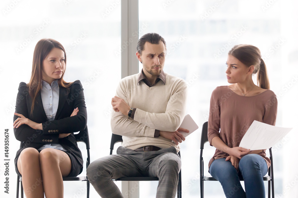 Male and female candidates waiting for interview, sitting together in a row, looking at each other with hate and dislike, feeling jealous envious, rivalry and competition while applying for a job Male and female candidates waiting for interview, sitting together in a row, looking at each other with hate and dislike, feeling jealous envious, rivalry and competition while applying for a job