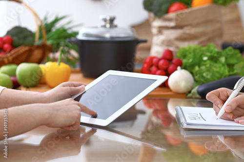 Human hands of two female persons using touchpad for making menu in the kitchen. Closeup of two women are making online shopping by tablet computer and credit card. Cooking and shopping concept