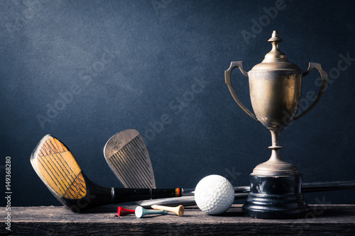 Fototapeta fotografia martwa: kij golfowy, piłka golfowa i koszulka ze starym trofeum mistrza na starym drewnie na ciemnym tle sztuki