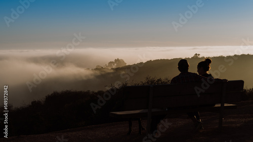 Couple sitting on bench talking over a foggy sunset together, relationship