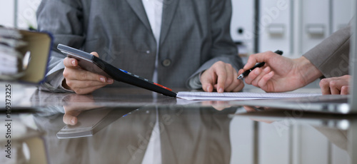 Two female accountants counting on calculator income for tax form completion, hands closeup. Internal Revenue Service inspector checking financial document. Planning budget, audit concept.