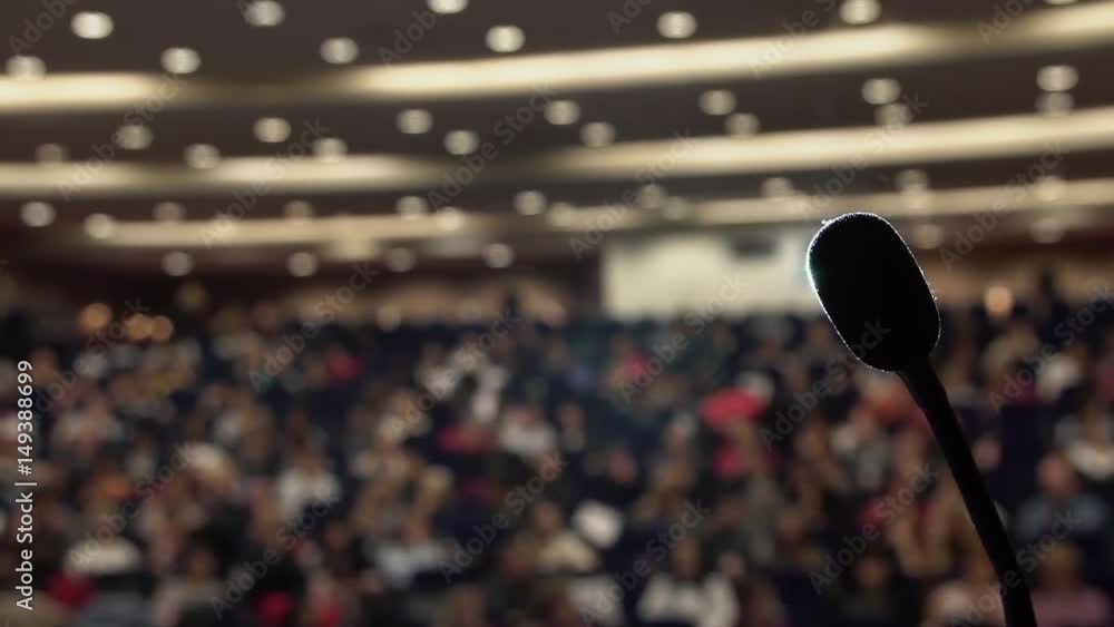 Many people sit in large hall at conference. Projector light via the microphone.
