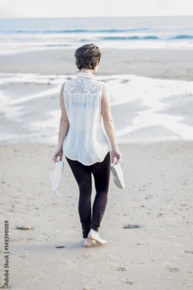 Chica andando por la orilla de la playa con camisa blanca