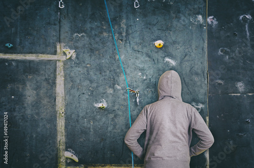 Rear view of hooded man against artificial rock climbing wall. © NatasaAdzic