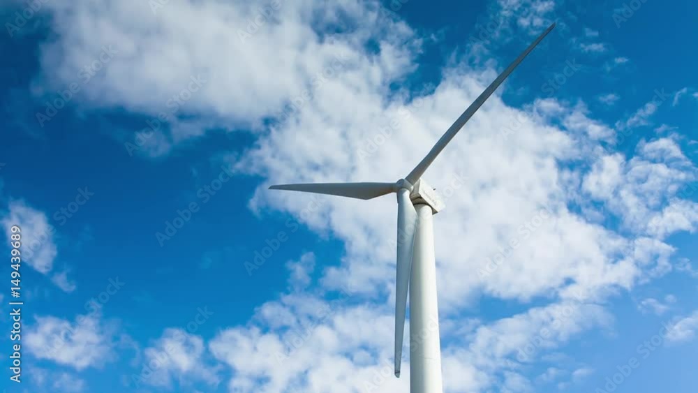 The blades of the wind station are spinning against the beautiful blue sky with feathery clouds on a sunny day. One wind farm is white. Wind energy. The blades of the wind station are spinning against the beautiful blue sky with feathery clouds on a sunny day. One wind farm is white. Wind energy.