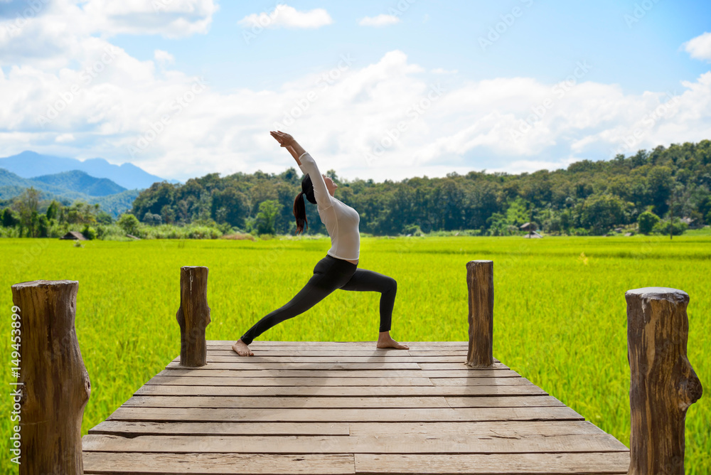 Healthy woman practicing yoga on the bridge in the nature, background rice field