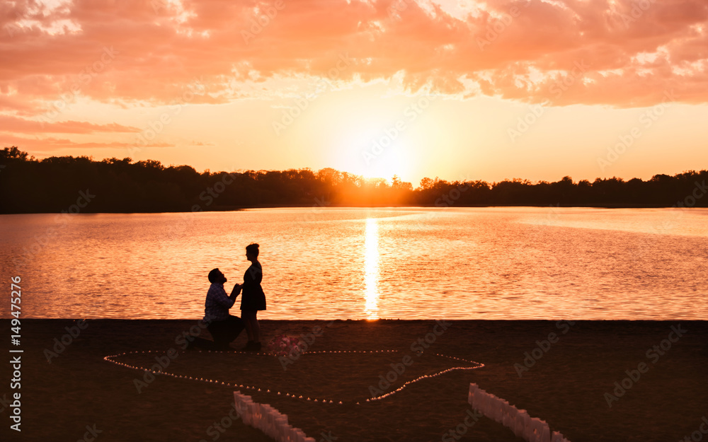 Fototapeta premium A man is proposing to his girl friend at a lake under sunset