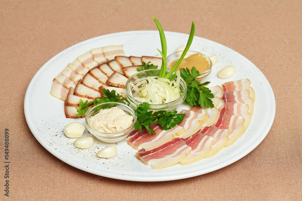 Strips of bacon and sliced lard, sauce, greens on plate Strips of bacon and sliced lard, sauce, greens on plate