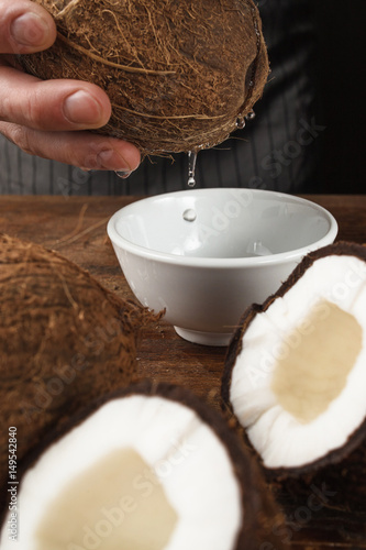 Fresh coconut milk pouring into white bowl on wooden table Preparing skin scrub, making massage oil, natural cosmetics concept