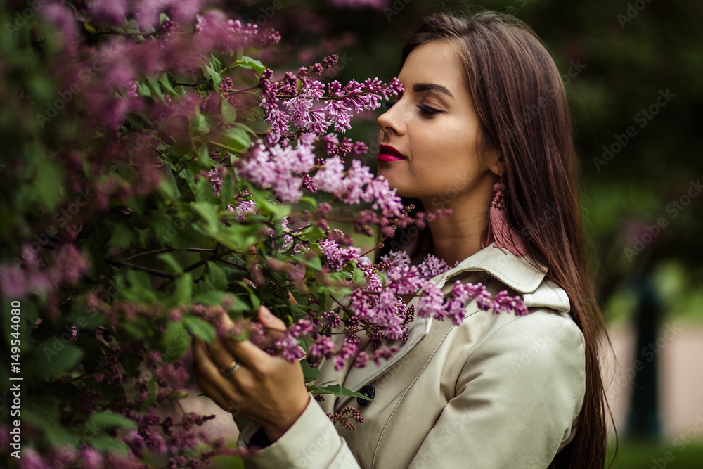 beautiful young woman in a trench coat near blooming lilac beautiful young woman in a trench coat near blooming lilac