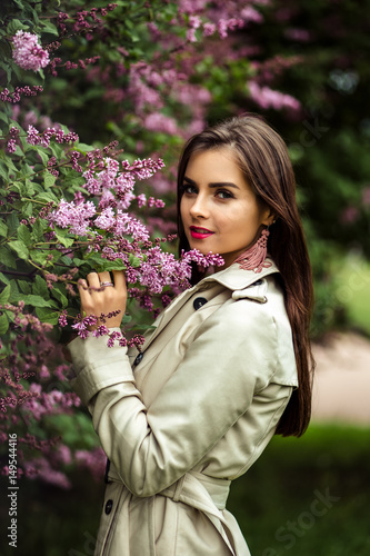 beautiful young woman in a trench coat near blooming lilac