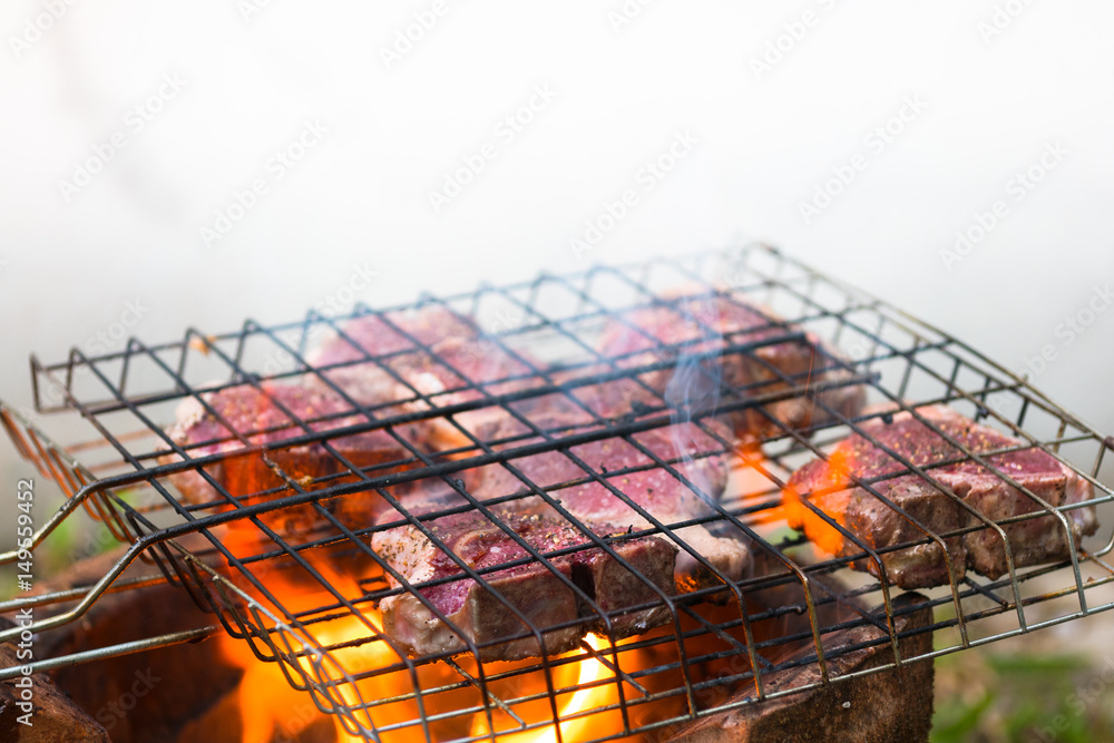 lamb grilled in grilling basket top of hot flame on charcoal stove with smoke, barbecue party