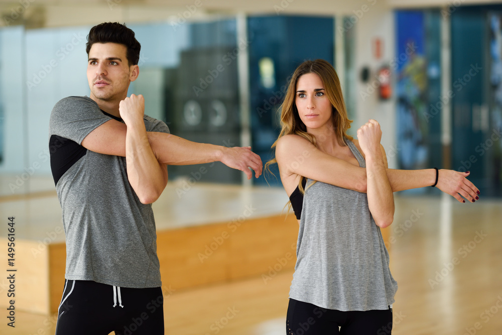 Two people stretching their arms in gym.