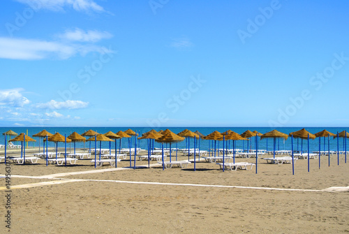 Summer holiday view of a Mediterranean beach prepared for a tourist season, a sandy beach by the blue sea, deckchairs, straw umbrellas and a wooden path at Torremolinos resort on Costa del Sol, Spain. photo
