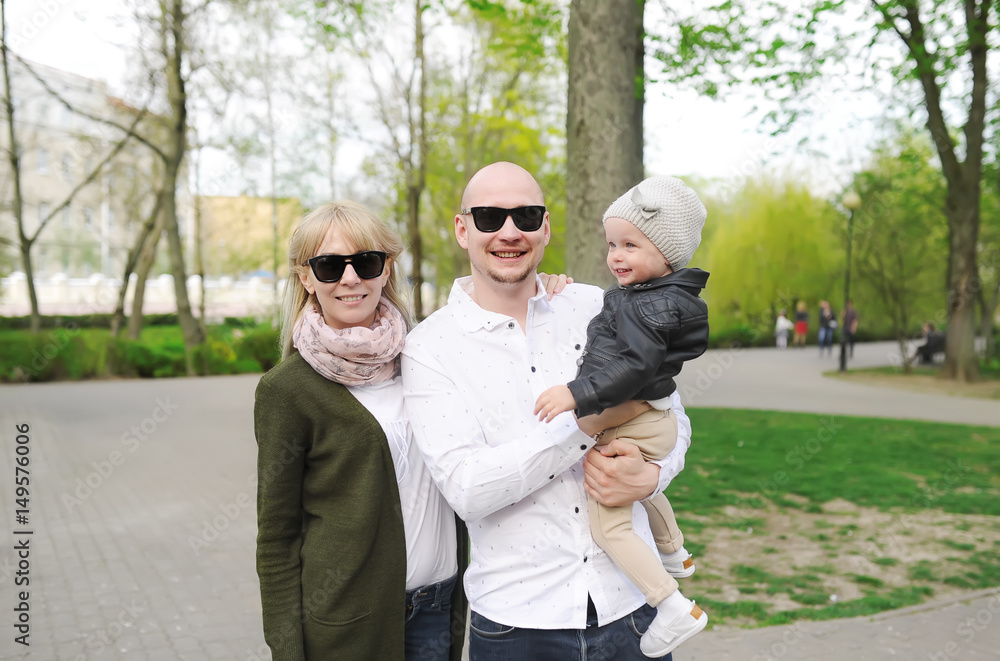 Young happy family in sunglasses of three having fun together outdoor. Pretty little daughter on her father back. Young happy family in sunglasses of three having fun together outdoor. Pretty little daughter on her father back.