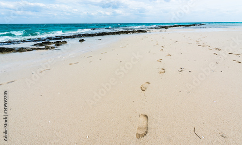 footprints on a sandy ocean beach with horizon on the background
