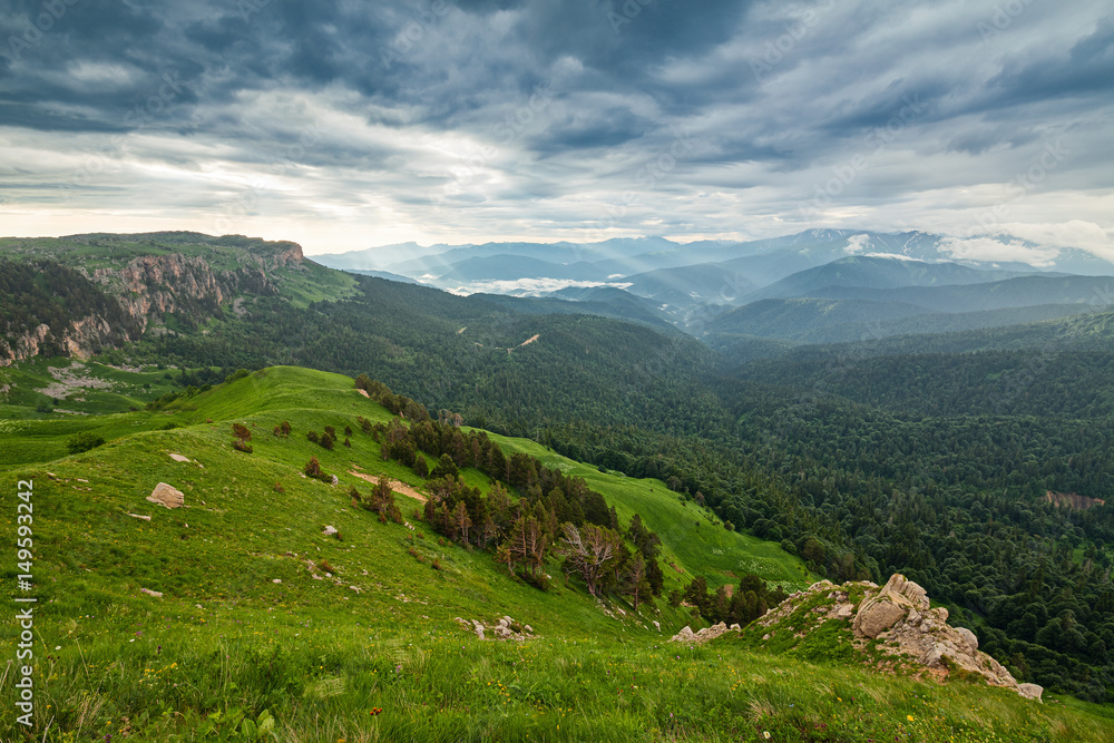 View on mountain forests and distant valley covered with glowing clouds and mist at sunset. Lagonaki, Caucasus, Russia