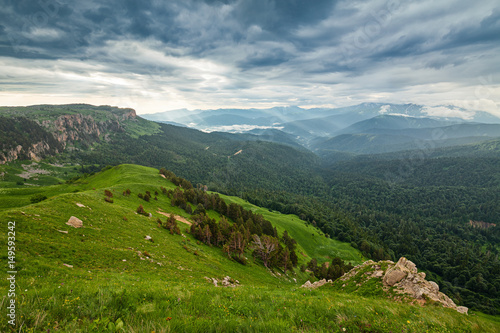 View on mountain forests and distant valley covered with glowing clouds and mist at sunset. Lagonaki, Caucasus, Russia