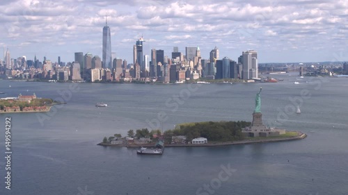 AERIAL ESTABLISHING SHOT: Flying around Lady Liberty statue in front of big New York City skyline. Famous Statue of Liberty standing proudly with New York downtown skyscrapers in the background