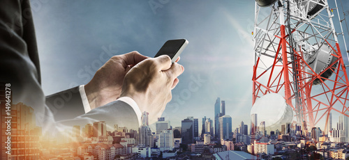 Businessman using smartphone with double exposure modern cityscape in sunrise, and telecommunication towers