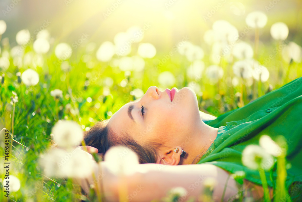 Beautiful young woman lying on the field in green grass and dandelions - obrazy, fototapety, plakaty 
