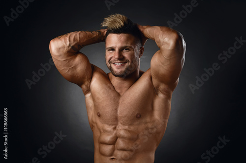 Studio portrait of topless muscular sportsman smiling over black background © niromaks