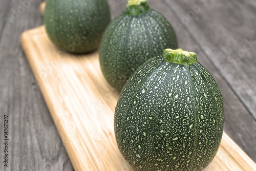 Round courgette on cutting board and on wooden background.