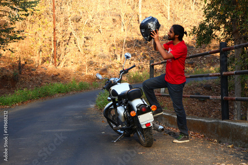 Young man standing near motorbike .
