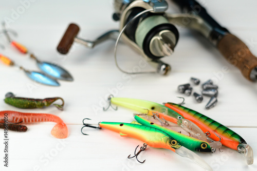 Fishing rod with reel, spoon baits, tackles and wobblers in box for catching or fishing a predatory fish on white vintage wooden background