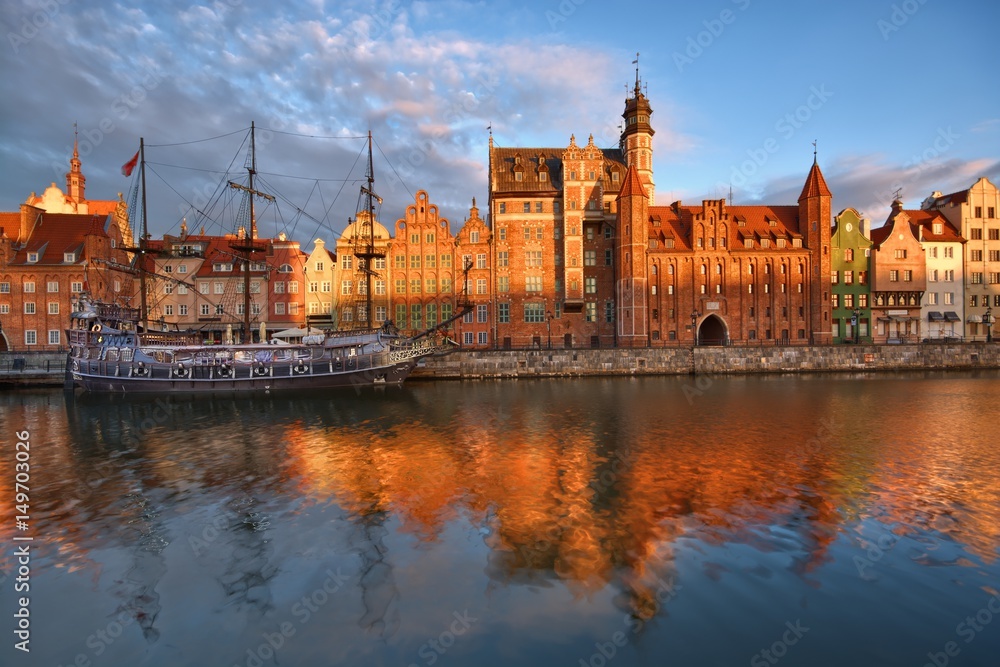 Caravel moored by Long Embankment on Motlawa River in the Old Town of Gdansk, Poland at sunrise. Mariacka Gate on the right
