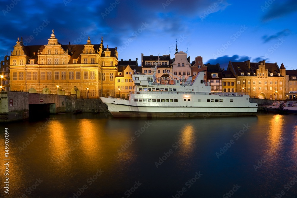 Ship moored by Long Embankment on Motlawa River in the Old Town of Gdansk, Poland at night. Illuminated Green Gate on the left