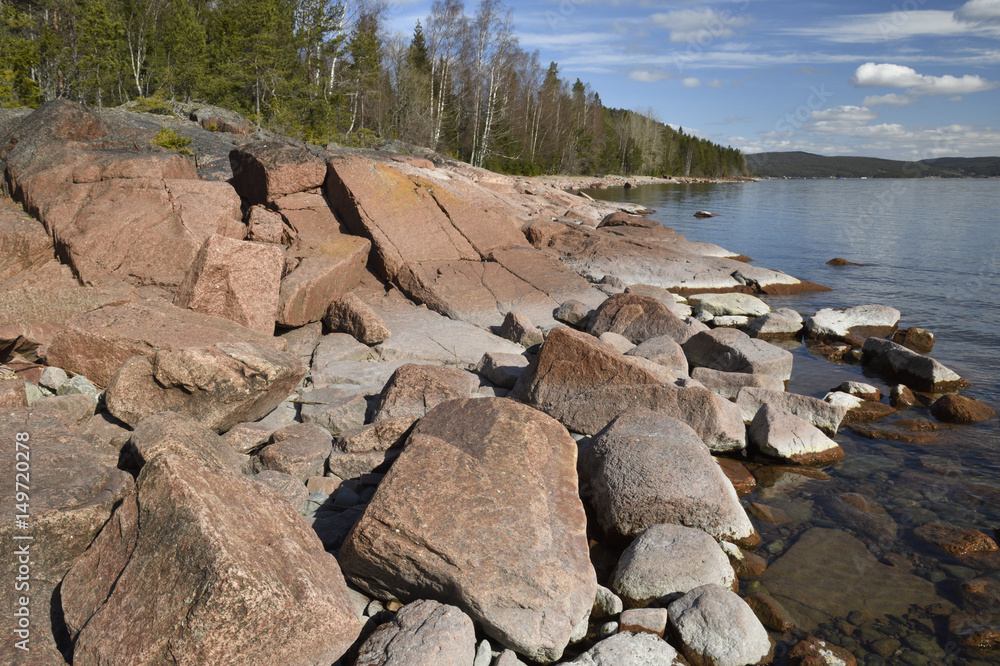 Sea shore with granite stones in foreground and forest in background