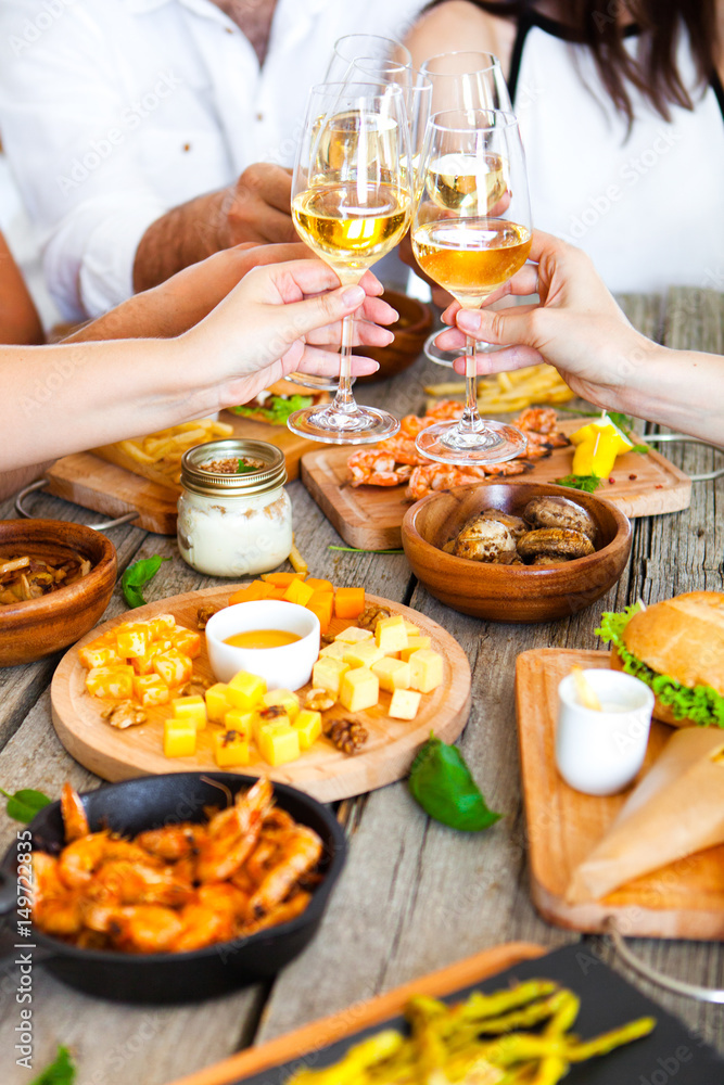 Hands with red wine toasting over served table with food. Hands with red wine toasting over served table with food.