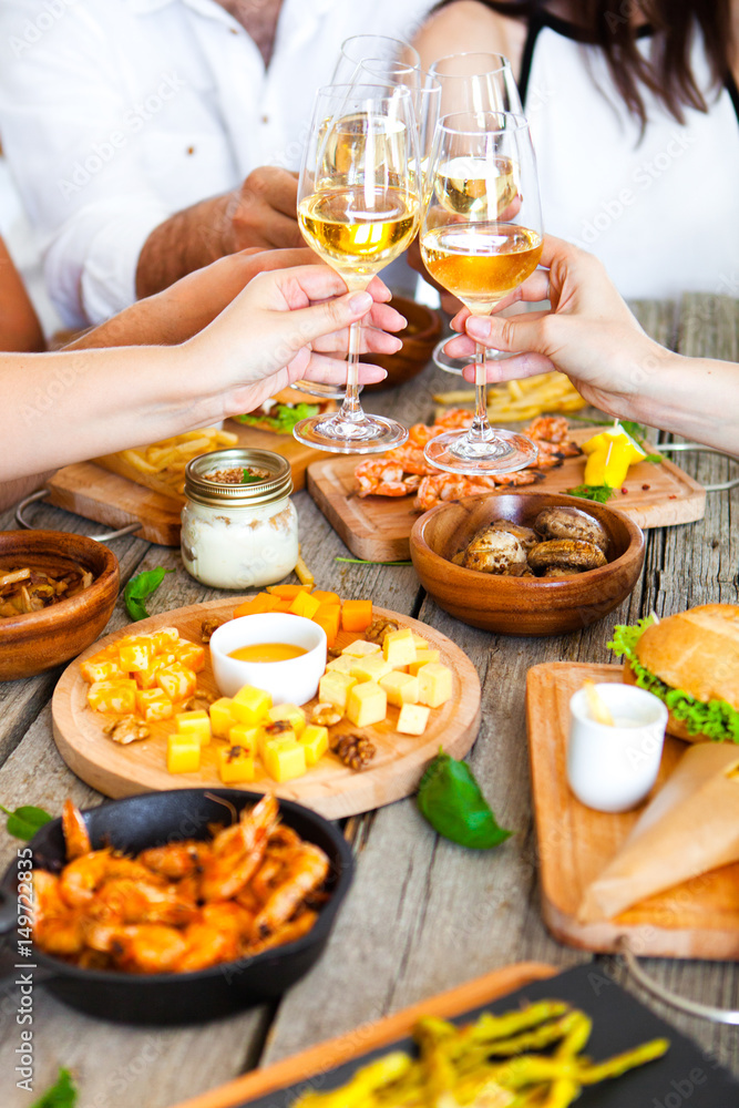 Hands with red wine toasting over served table with food.