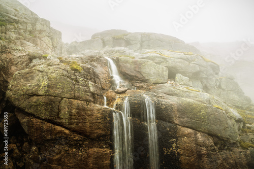 Small waterfall spilling out of rock gap, Norway majestic mist scenery, located by Kjerag famous natural landmark. Norway, Scandinavia, Europe. photo