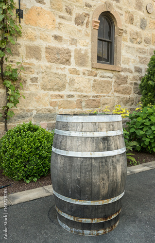 Old wooden wine barrel standing by stone wall of winery © steheap