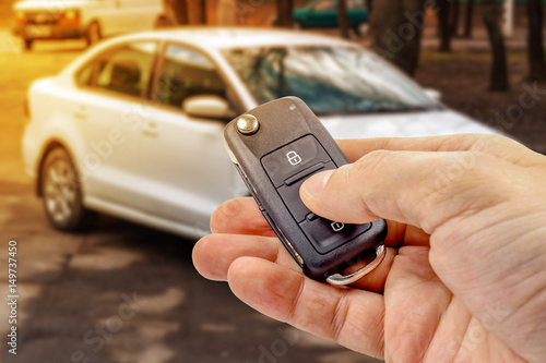 Man presses button on ignition key with immobilizer on the background of the car