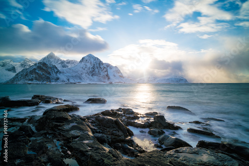 Sunrise on the stone shore of the ocean and mountains with snow on the horizon
