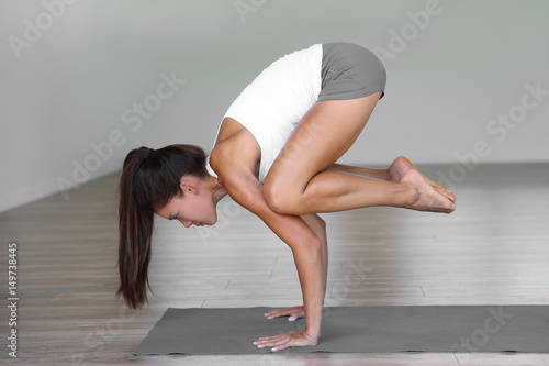 Yoga studio woman doing crow pose in fitness gym class. Girl training arms balance on exercise mat.