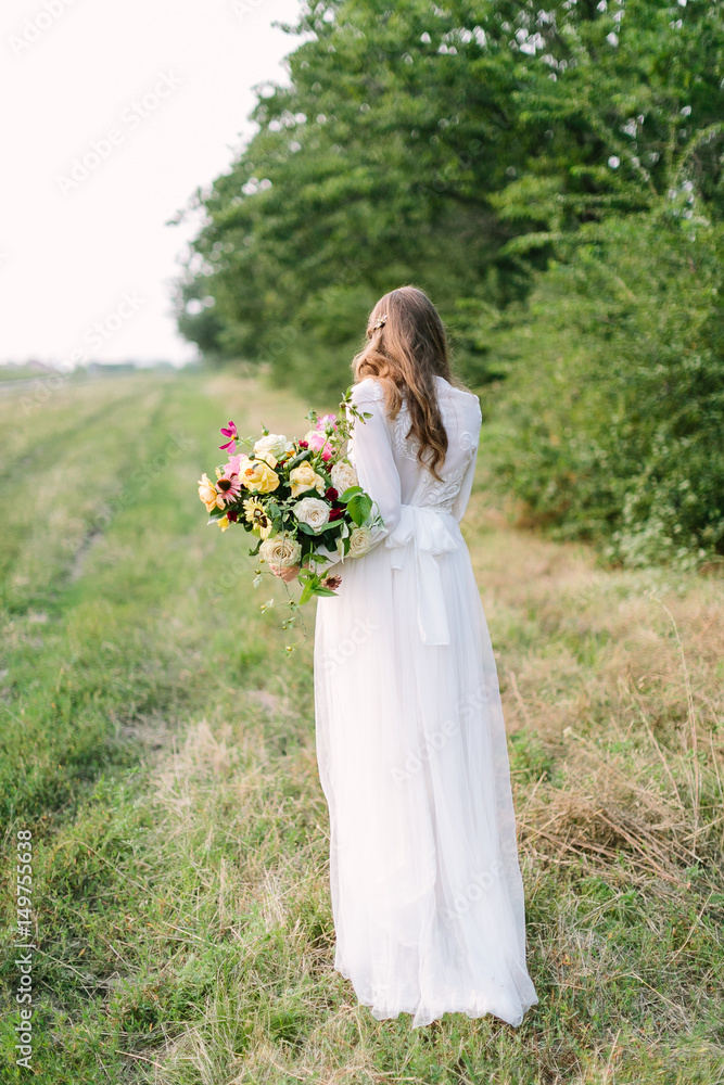 bouquet, people, flower holidays , gift and floral arrangement concept - beautiful female in a fashionable white dress posing with her back with bouquet of fresh flowers on background of trees