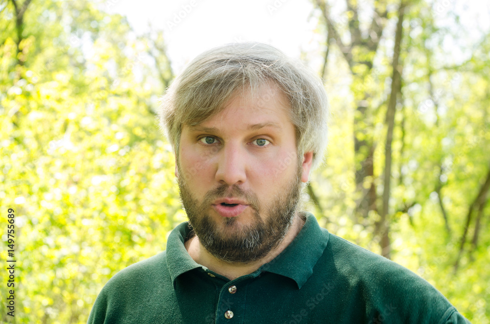 Portrait of an adult male with gray hair and beard talking and staring into the distance against the background of nature