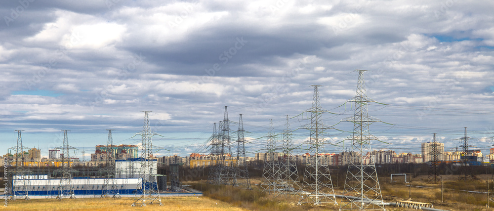 Industrial landscape. Electric wires, poles and power transformer plant. City and houses in background.