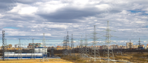 Industrial landscape. Electric wires, poles and power transformer plant. City and houses in background.