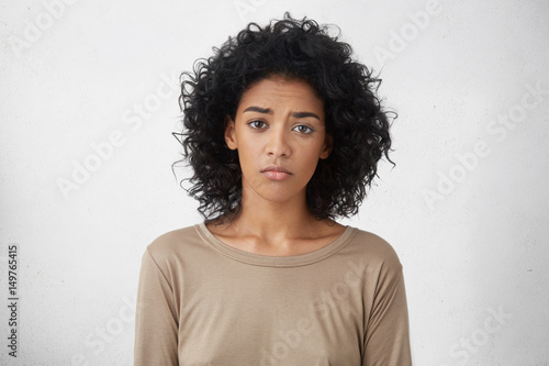 Fototapeta Attractive upset young dark skinned lady with Afro hairstyle feeling sad or bored expression while spending weekend at home, looking unhappy after friends forgot to invite her to party