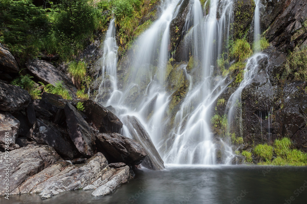 Long exposure of a waterfall with rocks and green during a sunny day