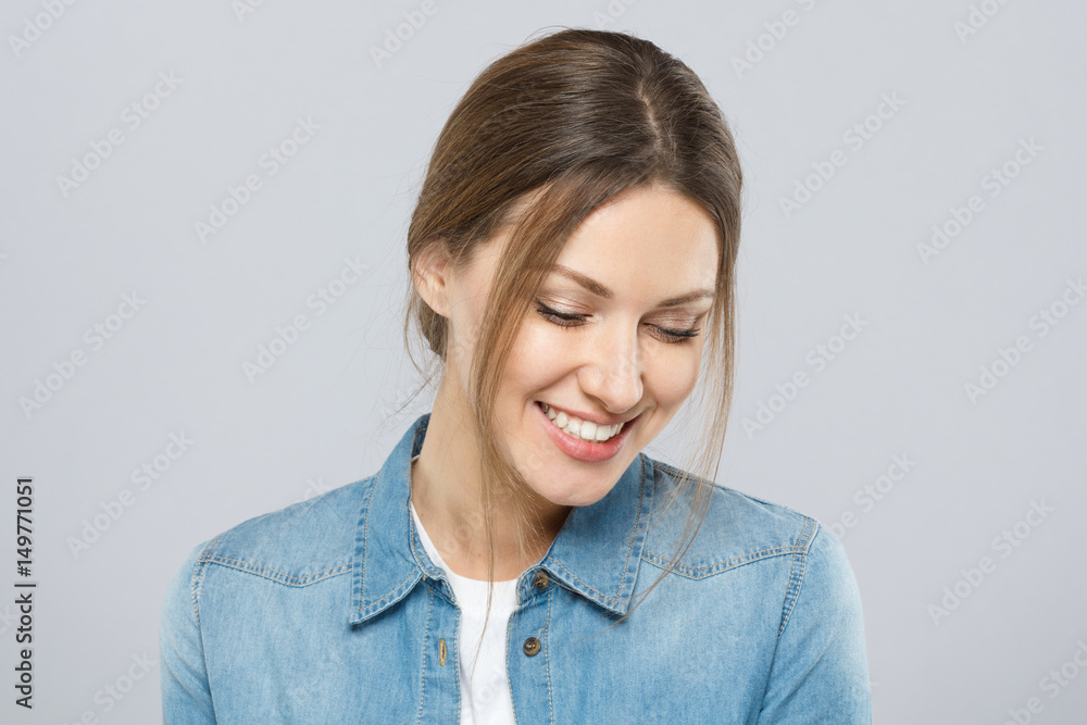 Obraz premium Photo of good-looking woman dressed casually isolated on gray background with eyes looking down in sign of modesty with light shy natural smile indicating pleasure, happiness and indecision.