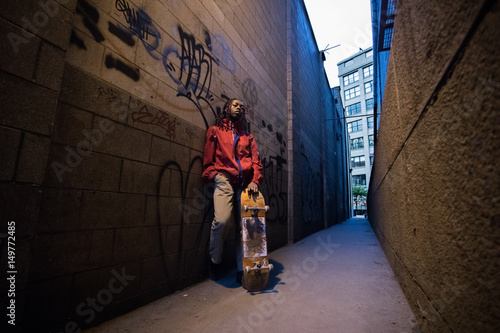 A young, african american skater girl poses with her skateboard in a back alley. Shot in DUMBO, Brooklyn during the Spring of 2017
