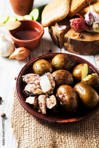 Russian and Ukrainian national cuisine, potatoes in their skin with fish, white bread, onions, garlic, cucumber and vegetable oil on a light wooden background 