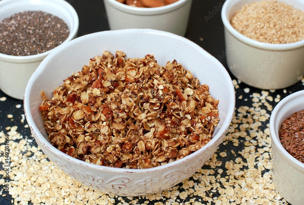 Homemade granola in white bowl with almond and seeds on black background Homemade granola in white bowl with almond and seeds on black background